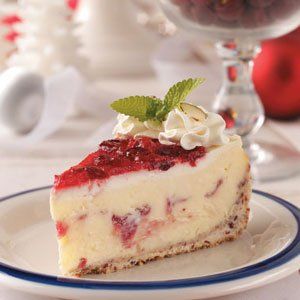 a piece of cheesecake on a plate next to a glass bowl with cherries