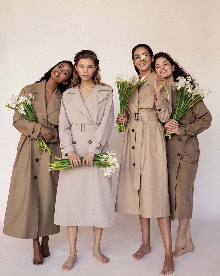 three women standing next to each other in trench coats and holding bouquets of flowers