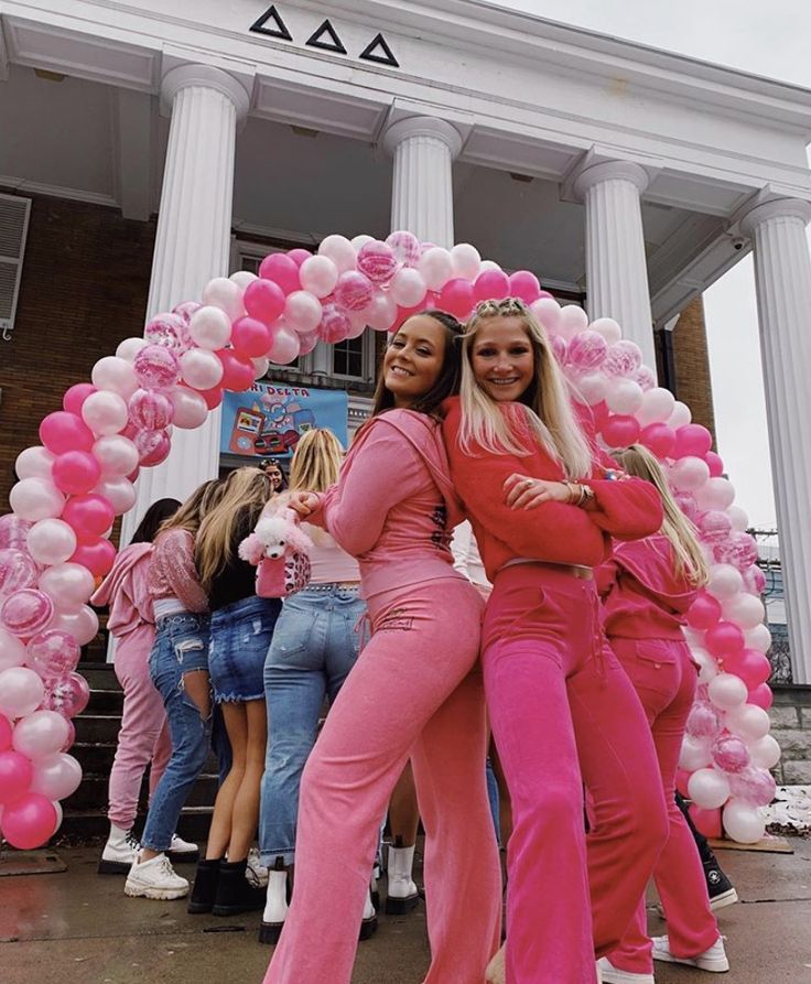 two women in pink outfits posing for the camera with balloons around them and an arch