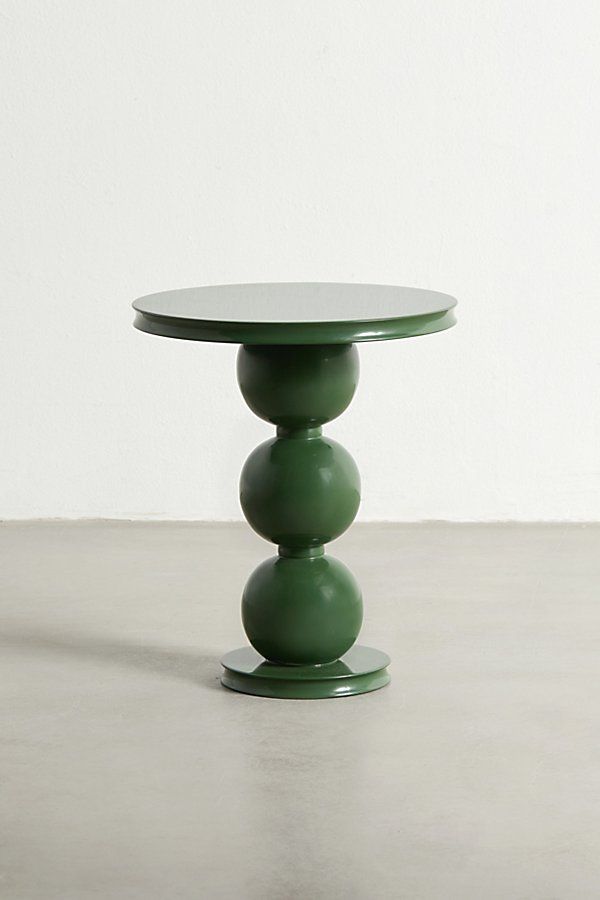 a green table sitting on top of a cement floor next to a white wall in an empty room