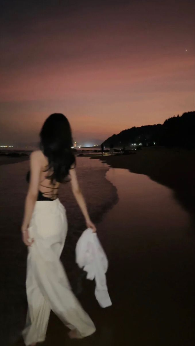 a woman is walking on the beach at night