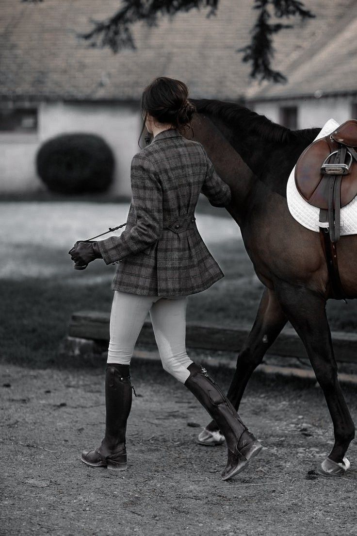 a woman is walking her horse outside in the evening hours and it looks like she's getting ready to ride