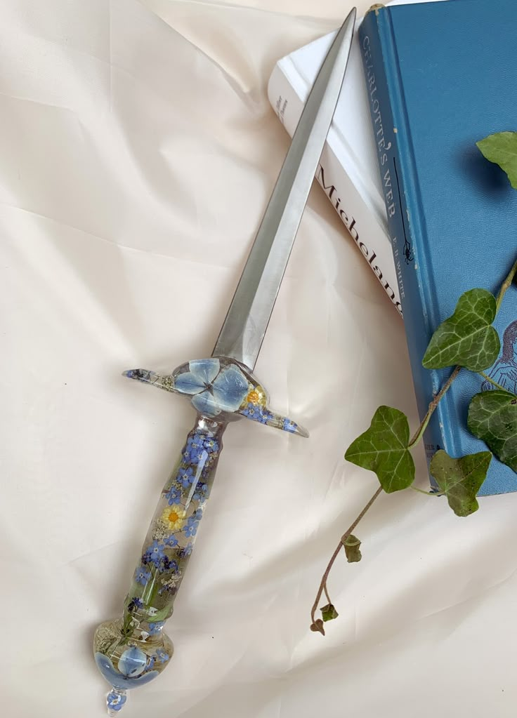 a book and a knife laying on a bed next to a plant with green leaves