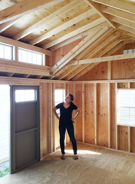 a woman standing in an unfinished room with wooden walls