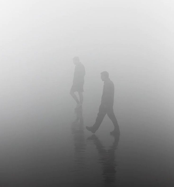 two people walking in the fog on a beach