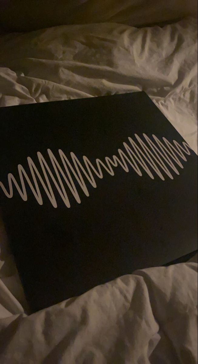 a black sign with white lines on it sitting on a bed next to a pillow