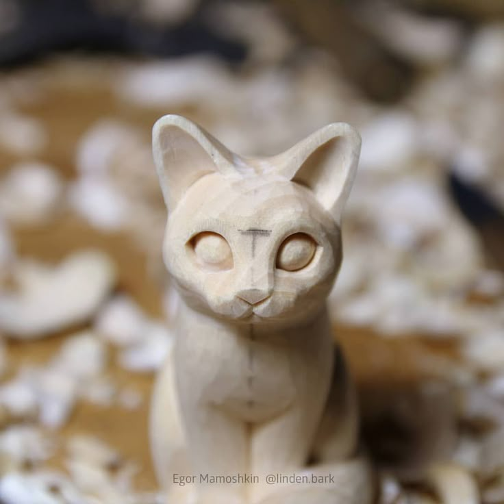 a white cat figurine sitting on top of a pile of wood shavings