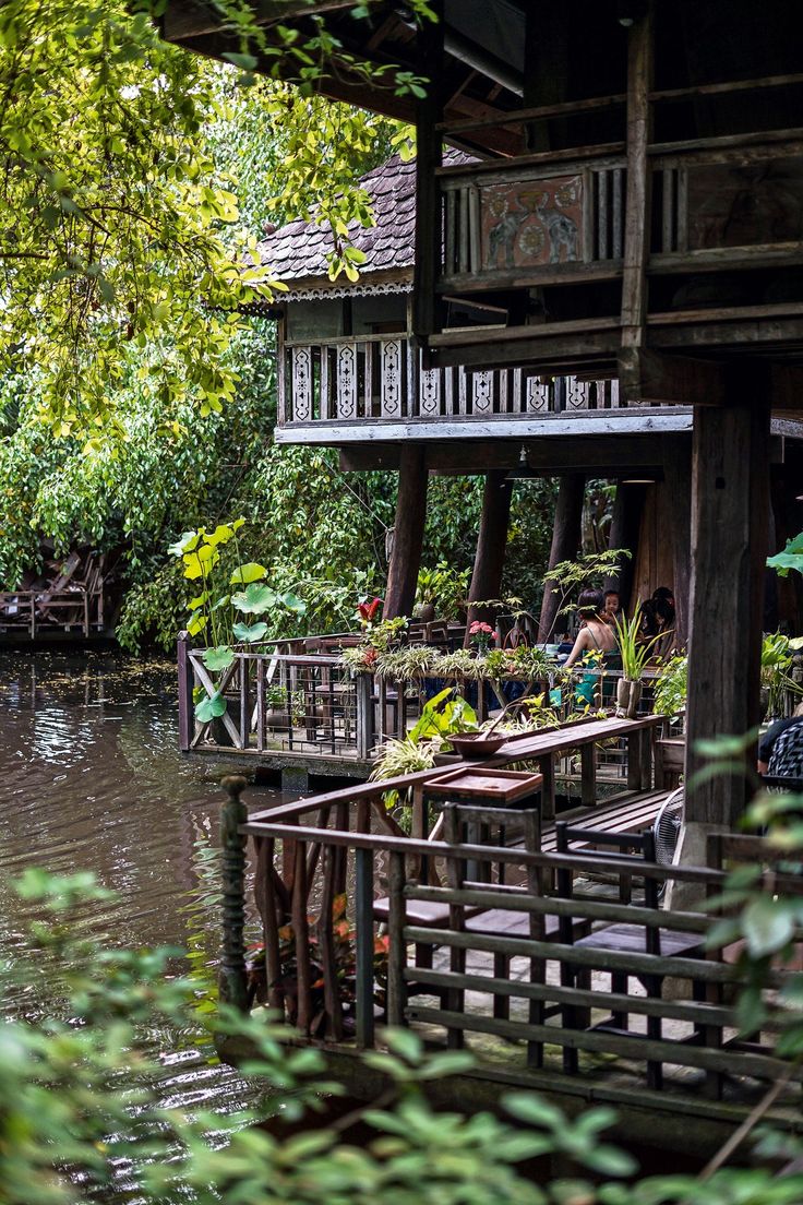 an old wooden house sitting on the side of a river next to a lush green forest