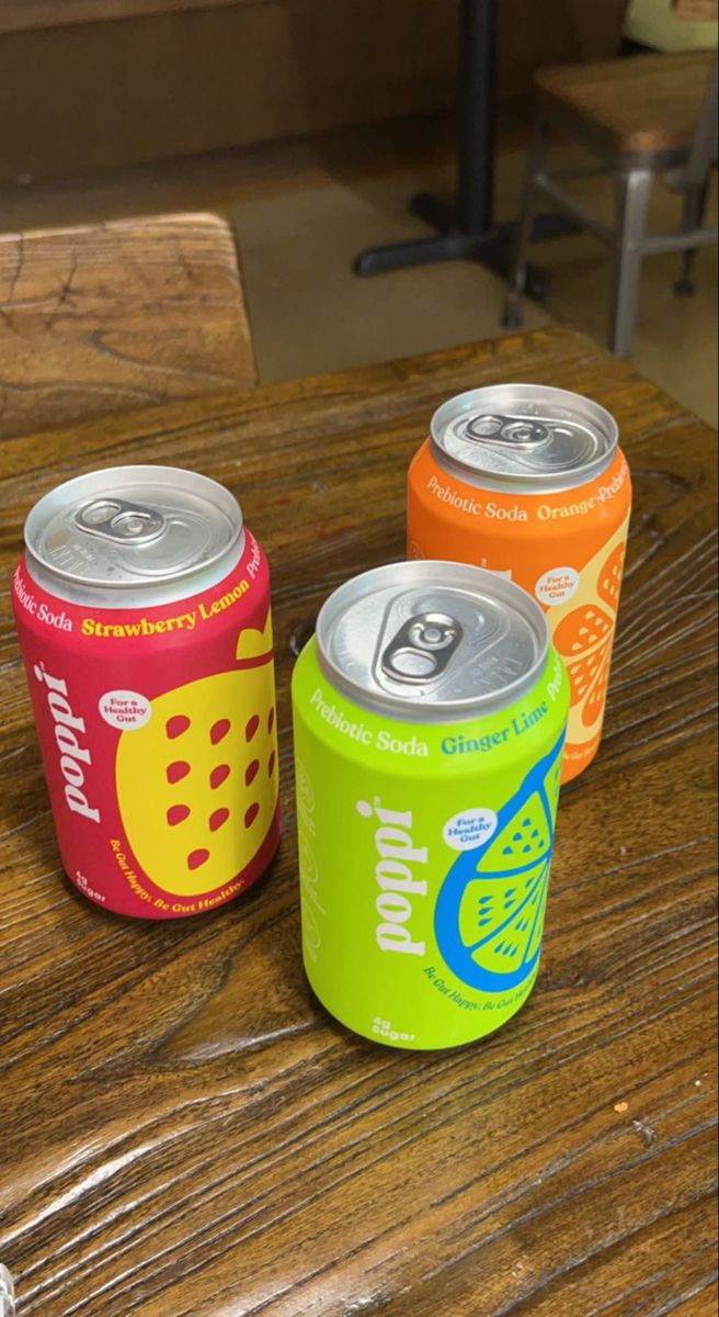 three soda cans sitting on top of a wooden table