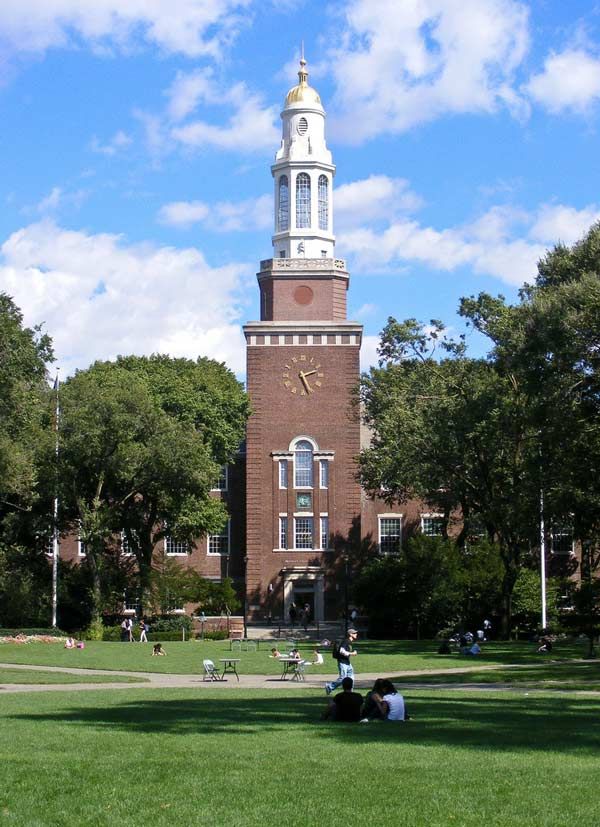 people sitting on the grass in front of a tall building with a clock at the top