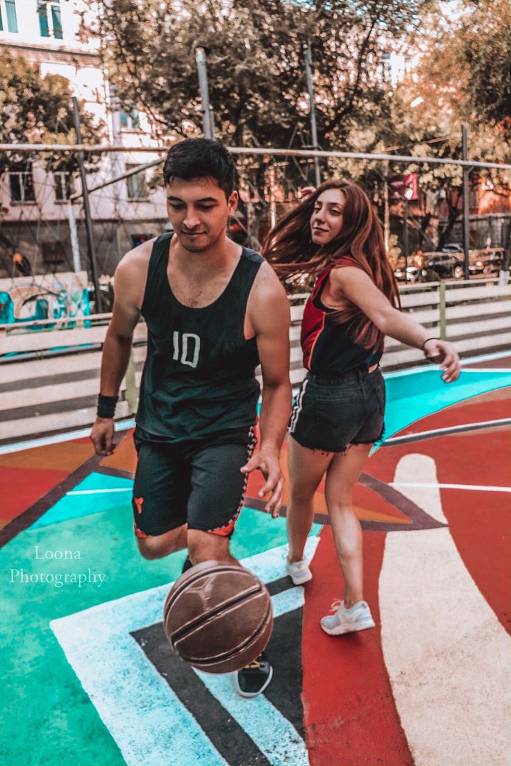 two young people are playing basketball on an outdoor court with painted lines and colorful paint