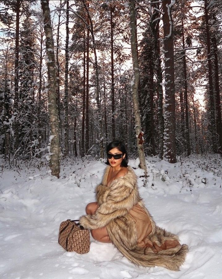 a woman in a fur coat sitting on the snow