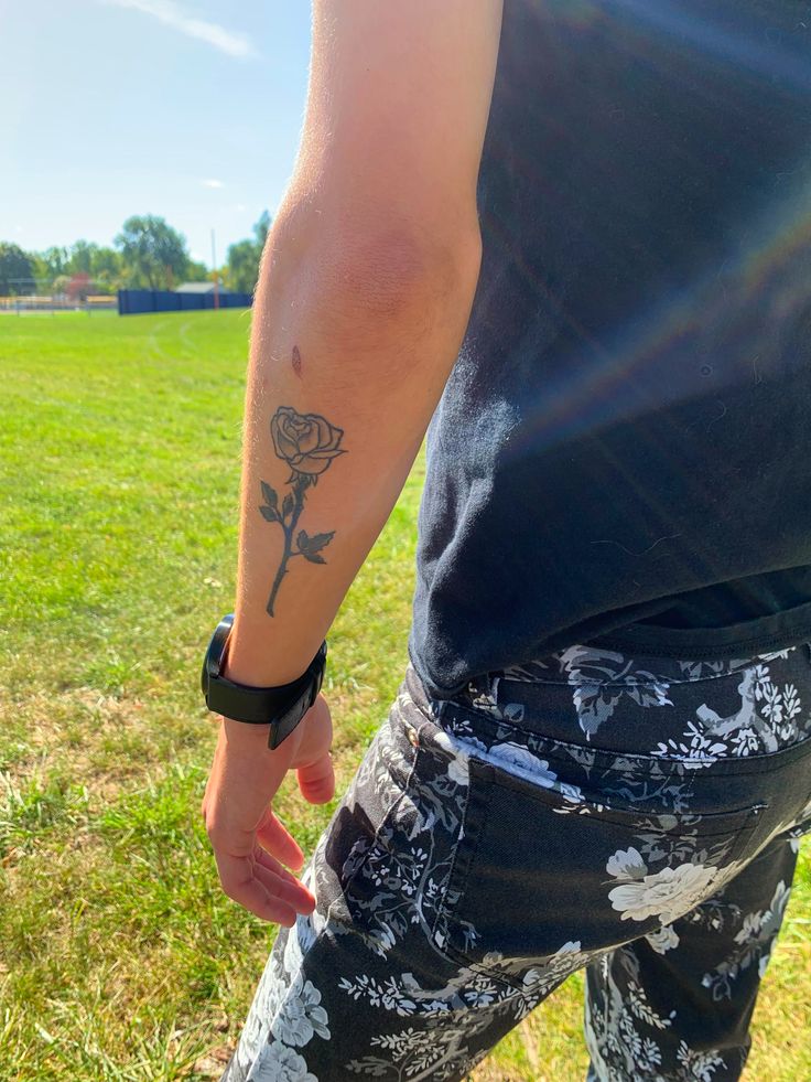 a man with a rose tattoo on his arm walking in the grass near a field