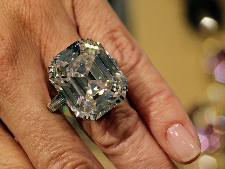 a close up of a person's hand holding a ring with a diamond in it