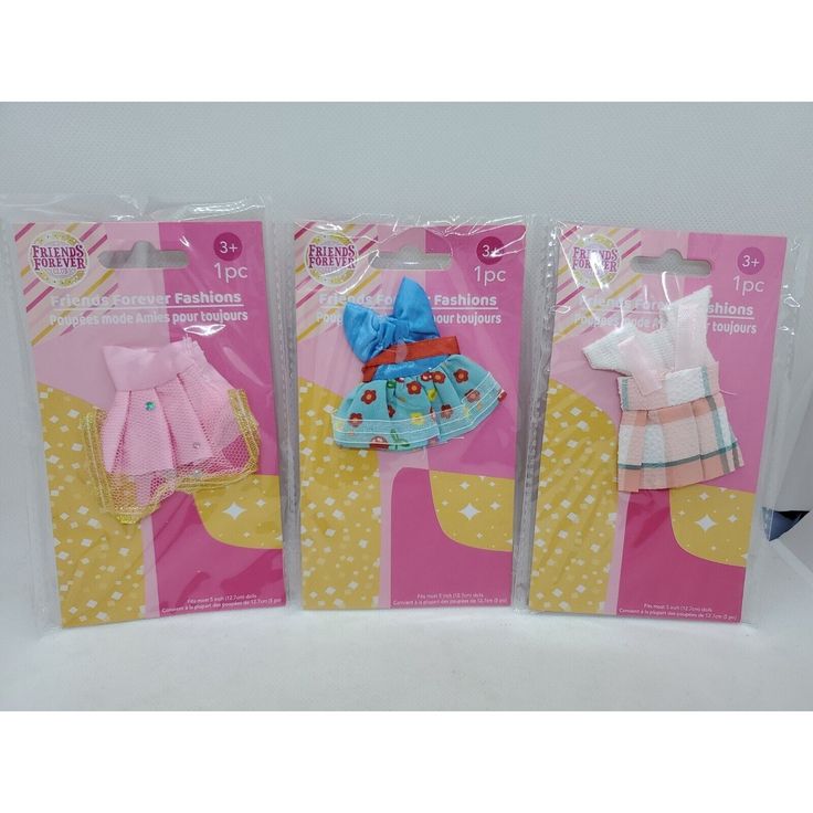 three packaged dolls in plastic packaging on a white tablecloth with pink and yellow polka dots