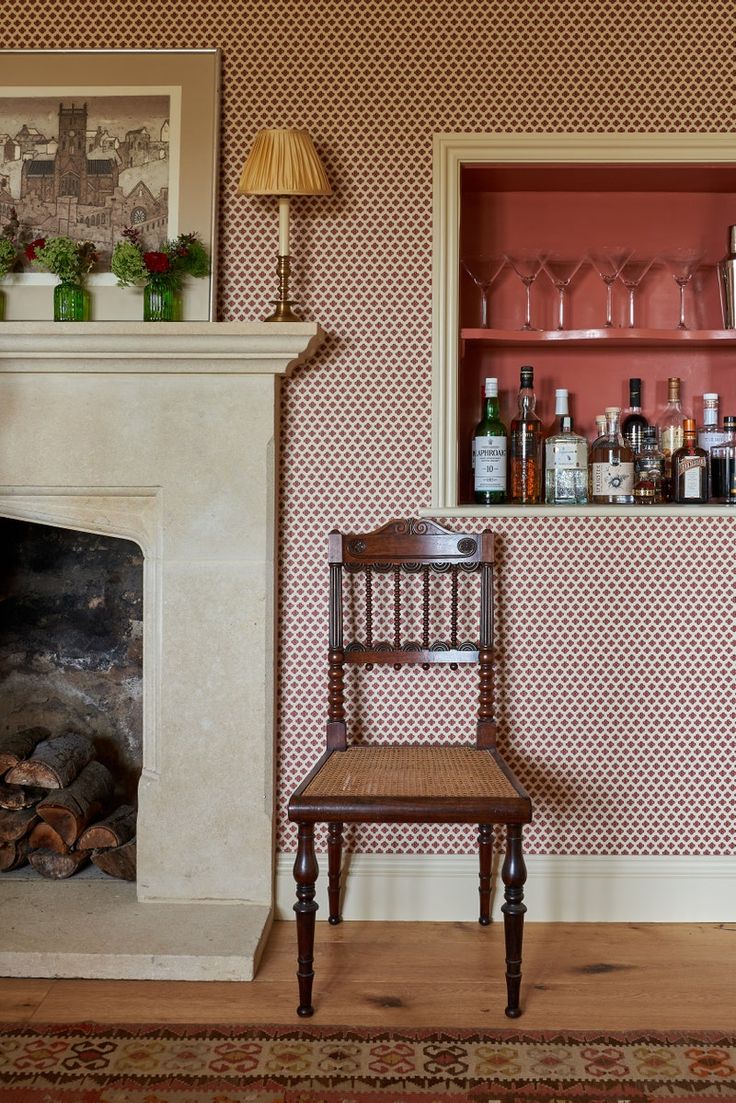 a chair sitting in front of a fireplace next to a shelf with bottles and glasses on it