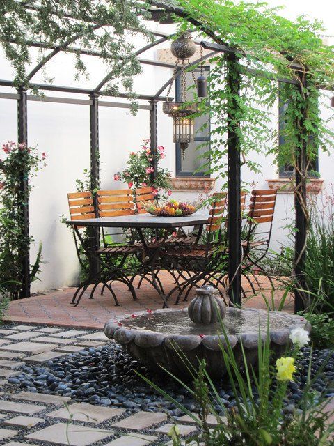 an outdoor dining area with table and chairs, surrounded by greenery on the patio