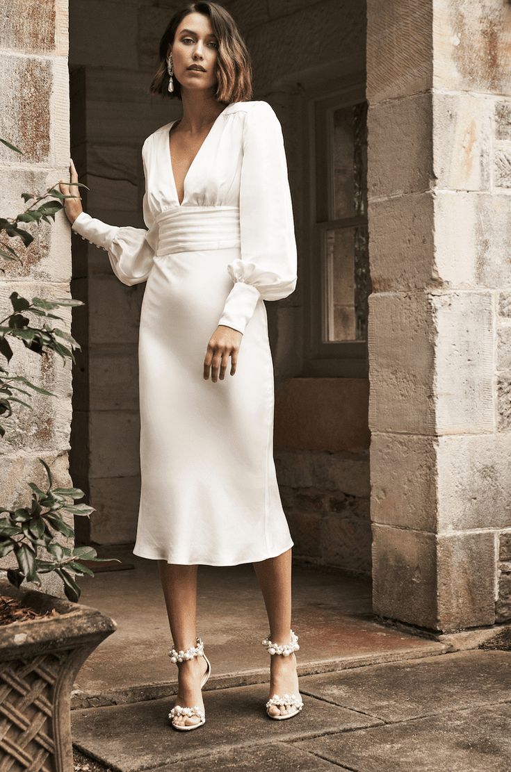 a woman in a white dress is standing outside