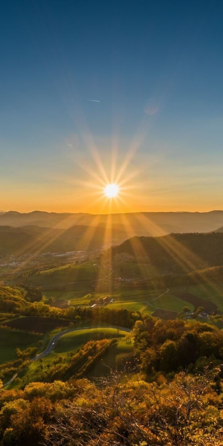 the sun is setting over a green valley