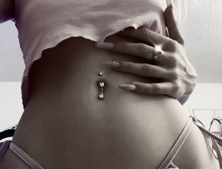 a woman's stomach with jewelry on it and her hands behind her back, in black and white