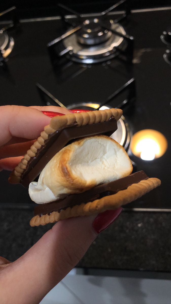 a hand holding a sandwich with chocolate and marshmallows on it in front of a stove