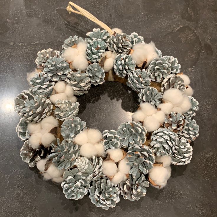 a wreath made out of cotton balls and pine cones on a granite countertop,