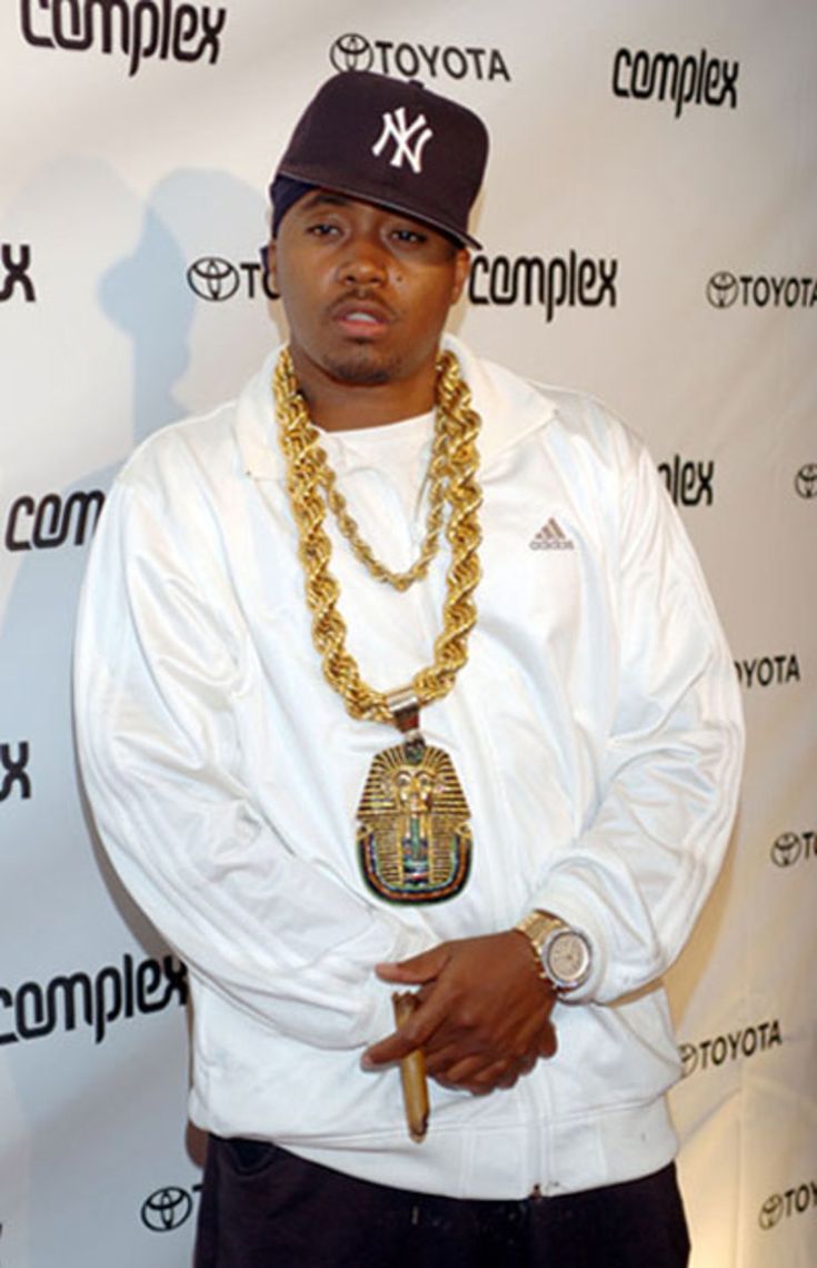 a man standing in front of a wall wearing a white shirt and gold chain necklace