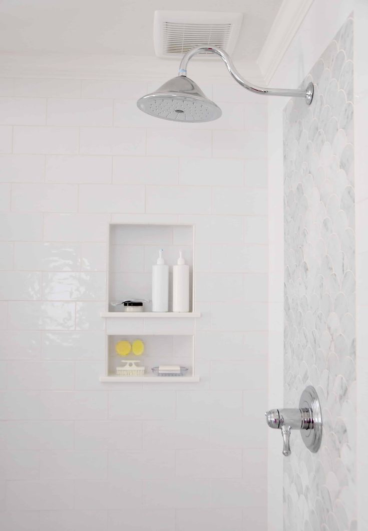 a shower head and shelves in a white tiled bathroom