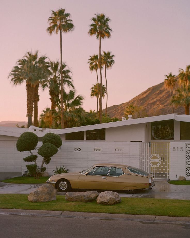 a car parked in front of a house with palm trees and rocks on the lawn