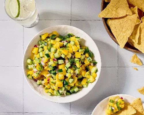 two bowls filled with corn salsa next to chips and a glass of water on the side