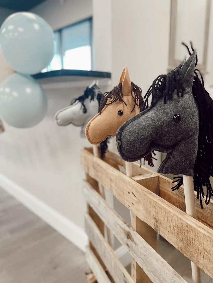 three horse head heads on top of wooden slats with balloons in the back ground