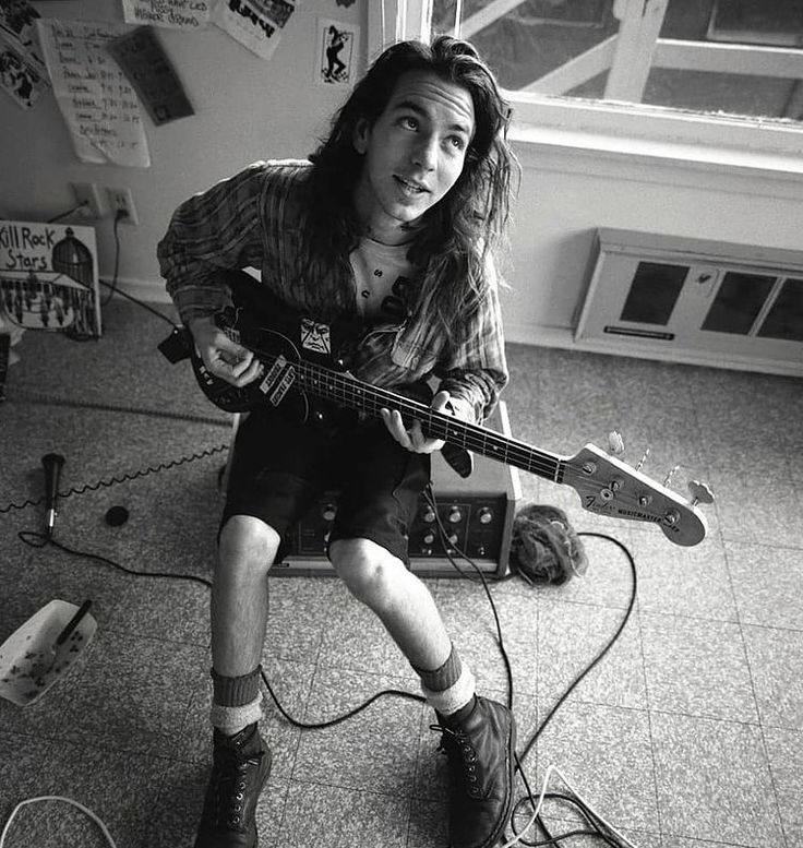 a woman sitting on the floor with a guitar in her hand and headphones around her neck