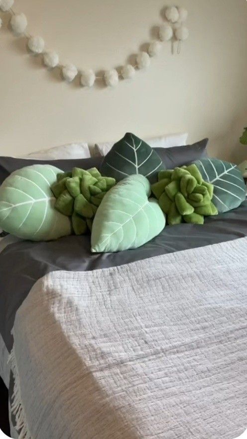 the bed is made with green leaves and pillows on it's sides, along with a string of pom - poms