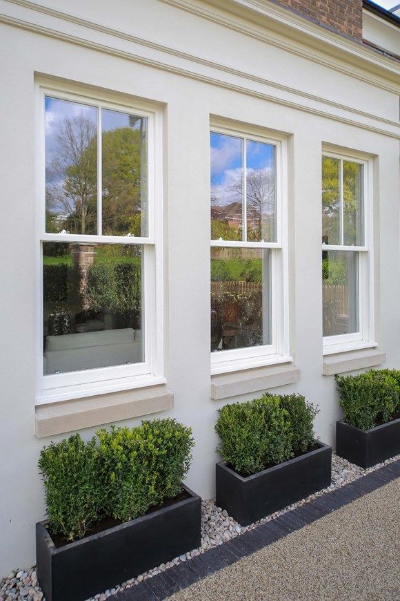 three black planters filled with green plants next to a white wall and windows on the side of a building