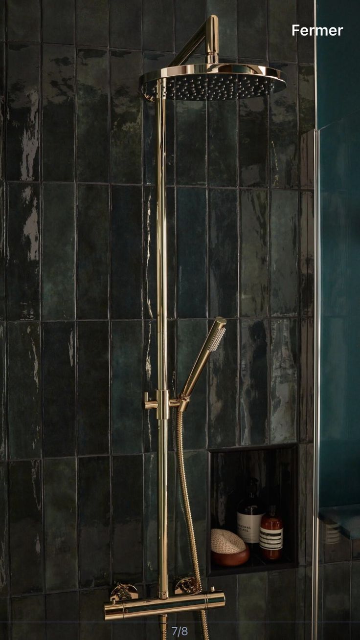 a gold shower head and handset in a green tiled bathroom with black tiles on the walls