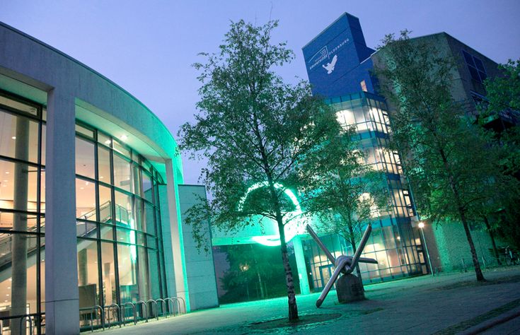 an illuminated building at night with trees in the foreground and green lights on it