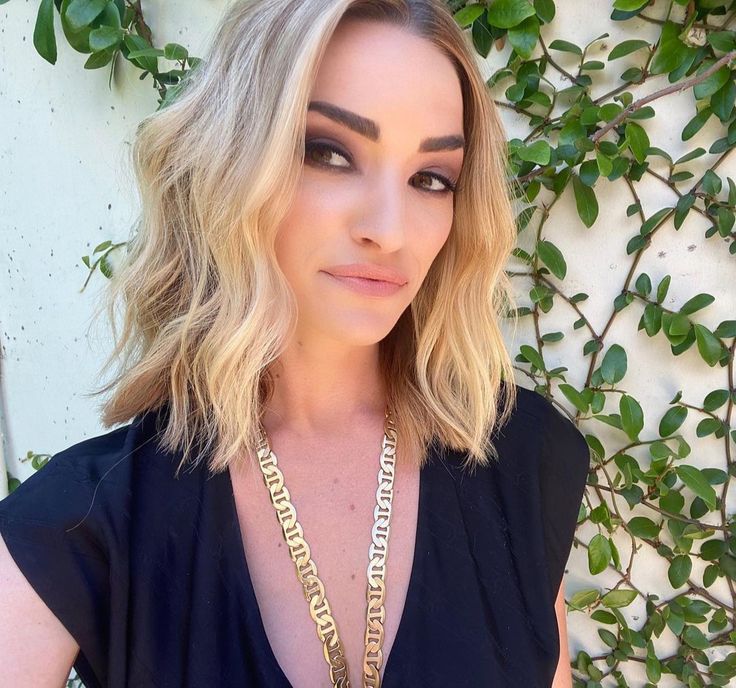 a woman with blonde hair wearing a black top and gold chains around her neck is looking at the camera