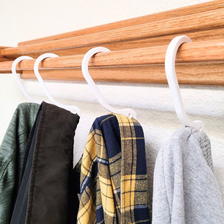 three coats hanging from a coat rack on a white wall next to a wooden rail