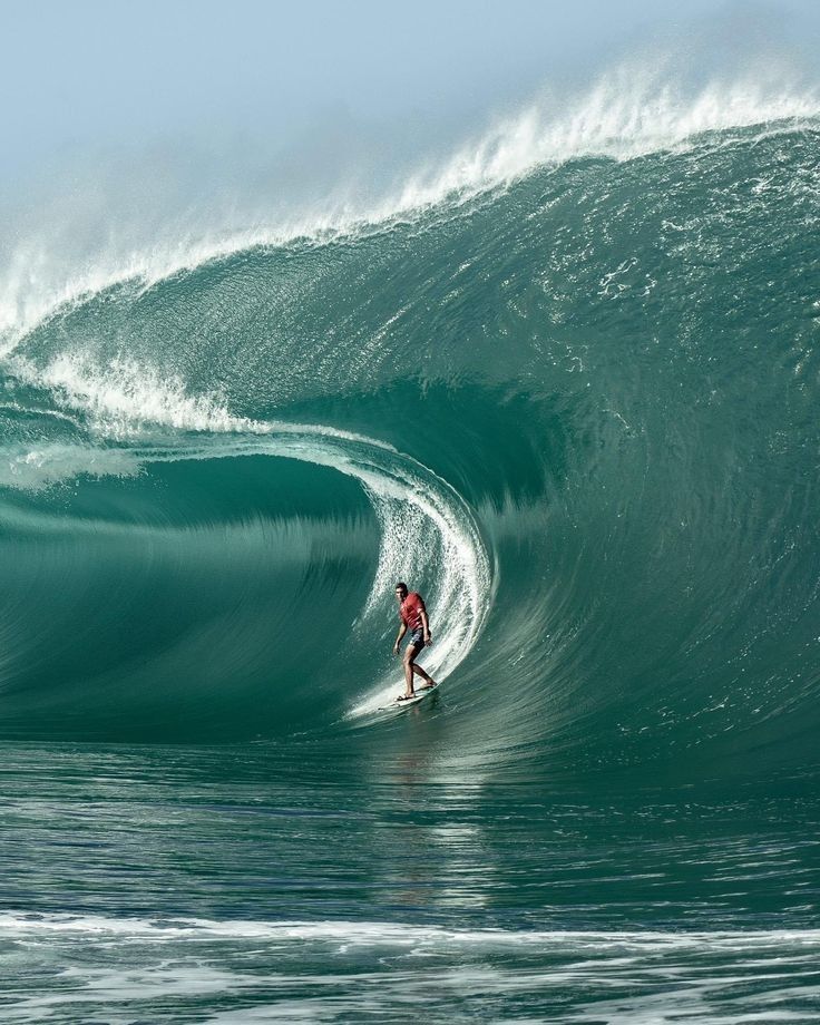 a man riding a wave on top of a surfboard in the ocean with large waves behind him