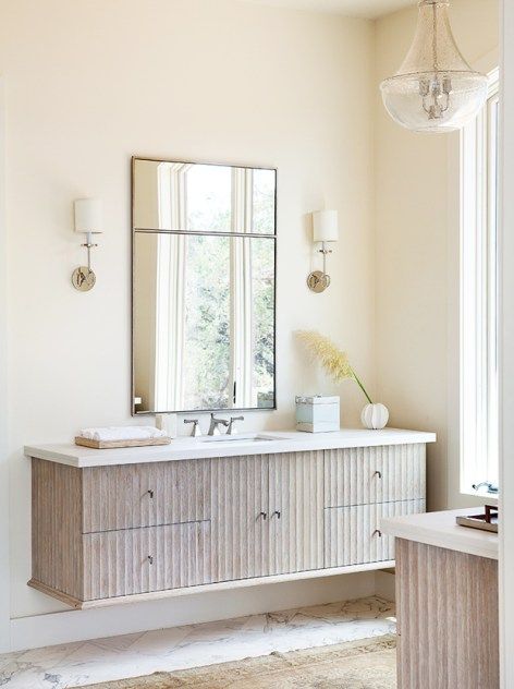 a bathroom vanity with two sinks and a large mirror above it, in front of a window