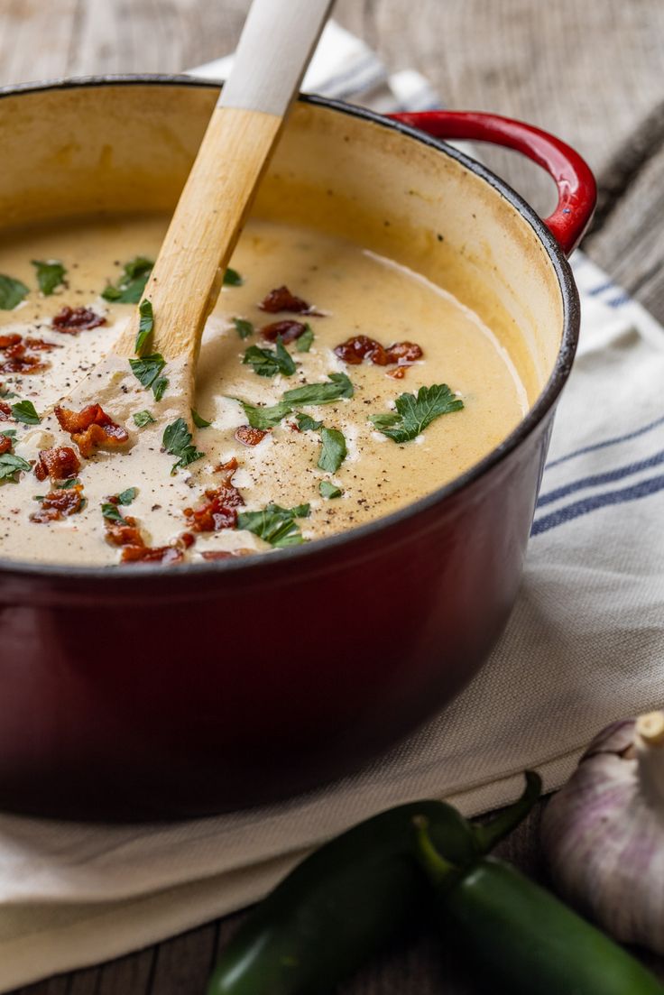 a red pot filled with soup sitting on top of a table next to green peppers