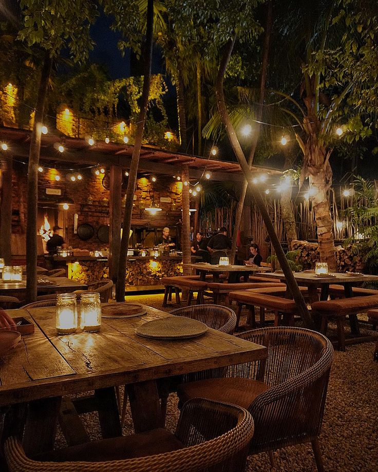 an outdoor dining area at night with lights on the tables and people sitting in chairs