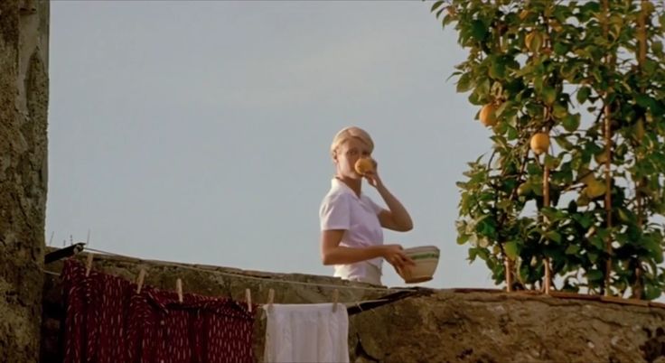 a woman sitting on top of a roof talking on a cell phone next to a lemon tree