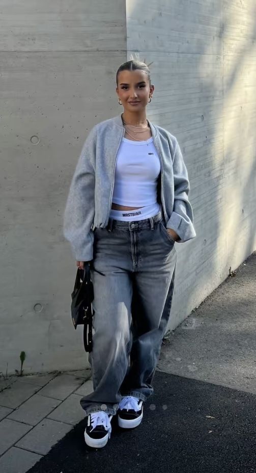 a woman standing in front of a white wall with her hands in her pockets and looking at the camera