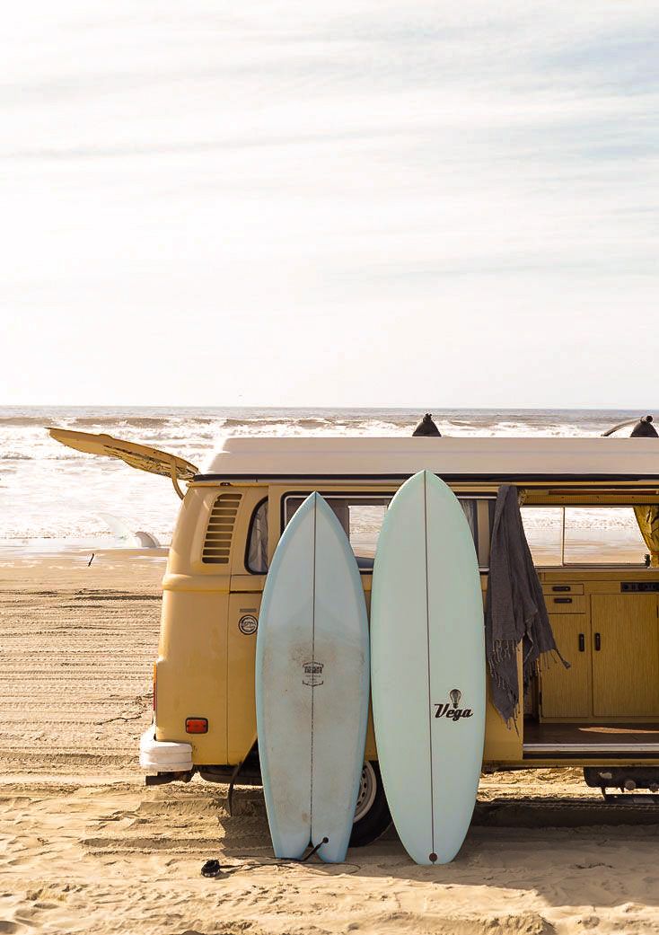 two surfboards are propped up against the back of a vw bus on the beach