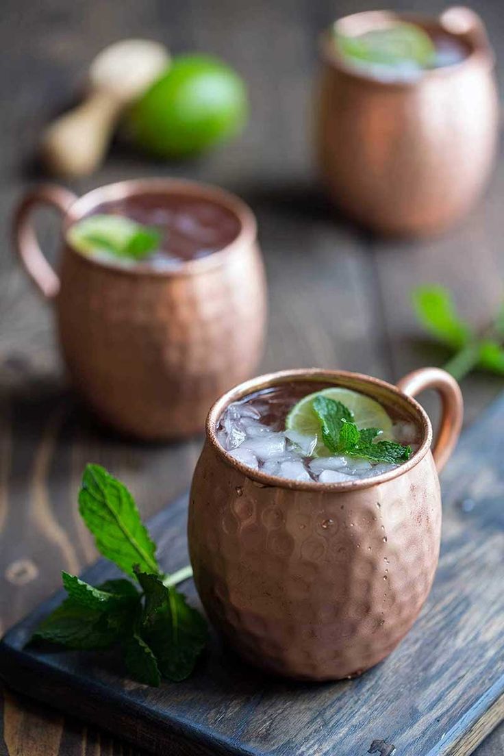 two copper mugs filled with ice and mint garnish on top of a wooden cutting board