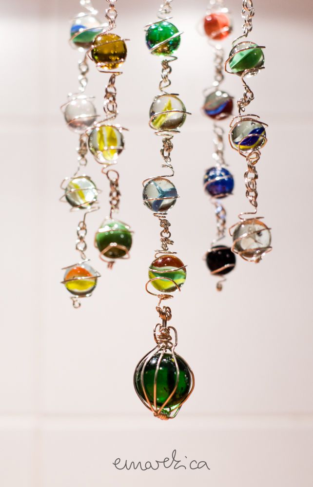 a multicolored glass bead hanging from a metal chain on a white wall