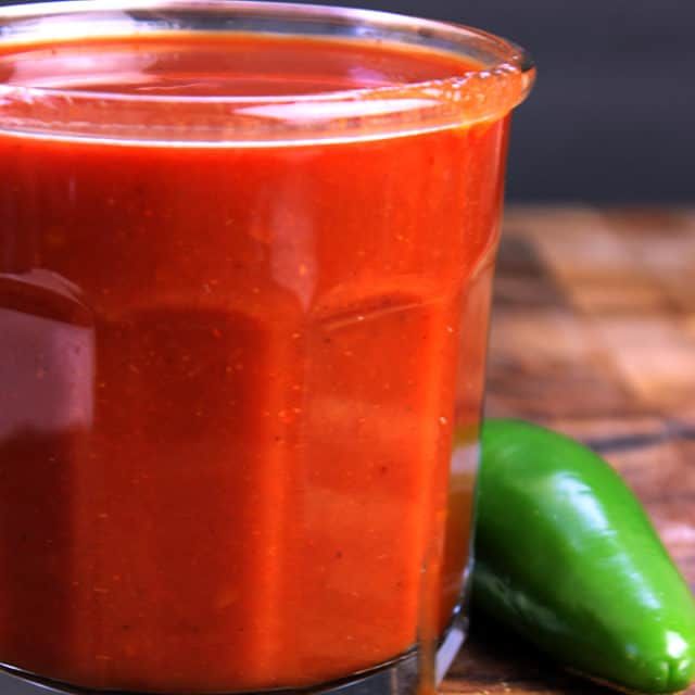 a jar filled with red sauce next to green peppers