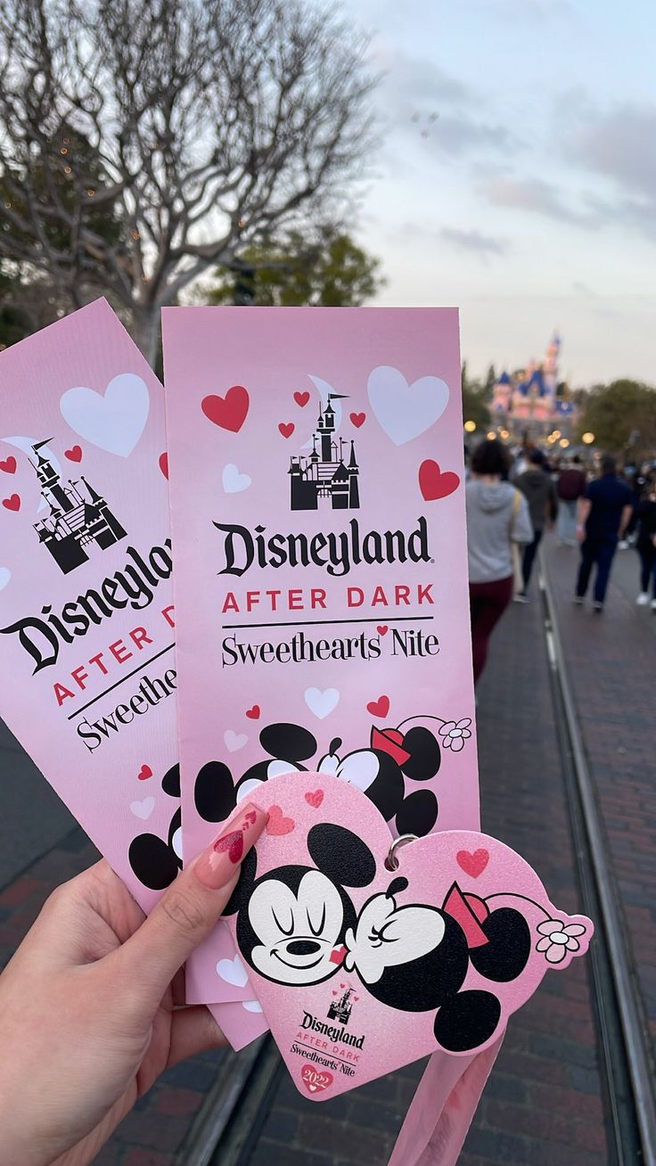 someone is holding up some pink disneyland after dark tickets for their trip to disney world