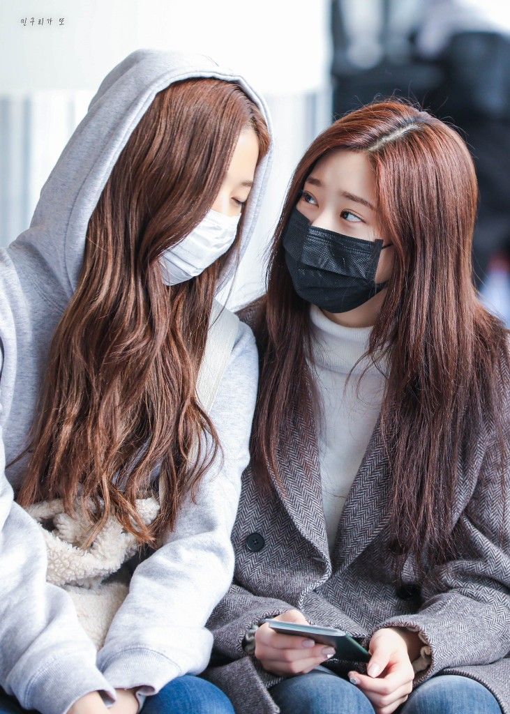 two young women wearing face masks while looking at their cell phones